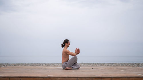 Side view of woman sitting on beach against sky