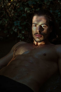 Portrait of shirtless wet young man lying in lake