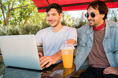 Smiling men using laptop sitting outdoors