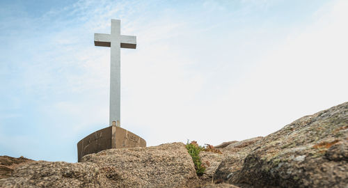 Low angle view of cross on rock against sky