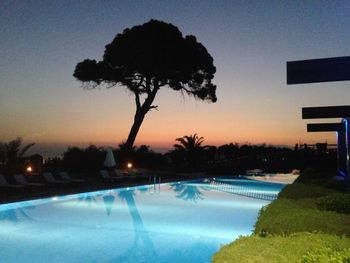 Silhouette trees by swimming pool during sunset