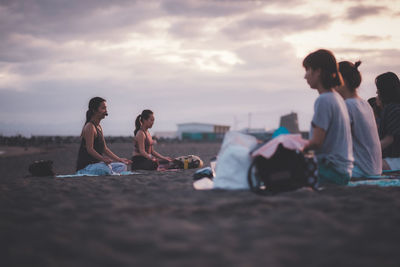 People relaxing on beach against sky during sunset