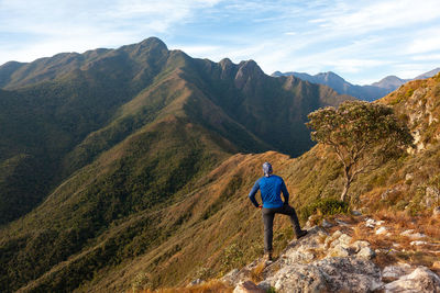 Rear view of man standing on mountain against sky