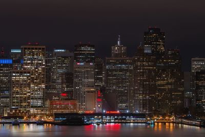 Illuminated buildings by river against sky at night