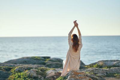 Woman standing on rock by sea against clear sky