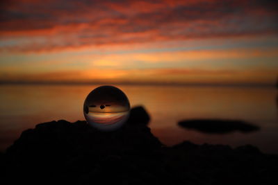 Silhouette rock on beach against sky during sunset
