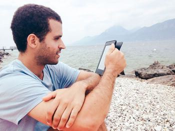 Young man using mobile phone at beach against sky
