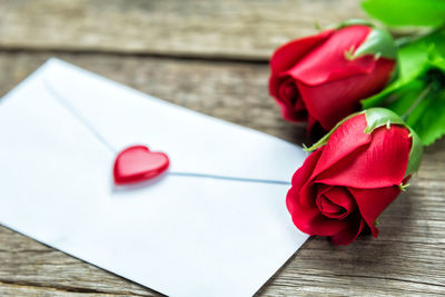 High angle view of red roses and envelope on table