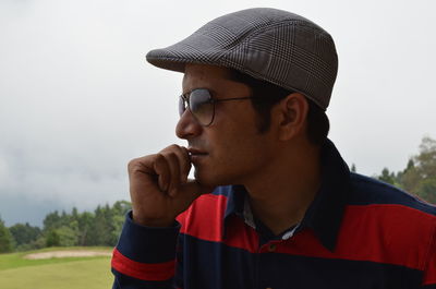 Man wearing sunglasses and cap while looking away against sky