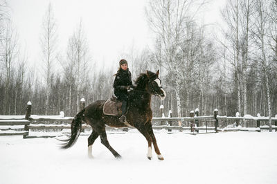 Woman riding horse on snowy field during snowfall