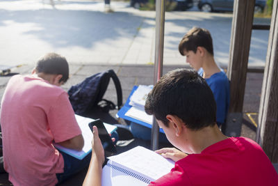 High angle view of friends studying while sitting on footpath during sunny day