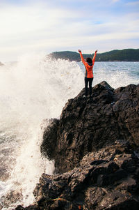 Woman standing on rock by sea against sky