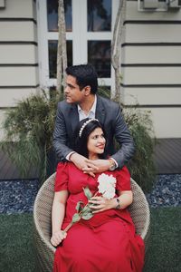 Thoughtful man with happy pregnant girlfriend sitting on chair