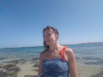 Young woman smiling at beach against blue sky