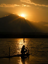 Silhouette people on boat on sea against sky during sunset