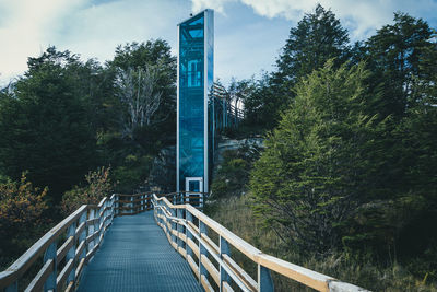 Footbridge amidst trees in forest against sky