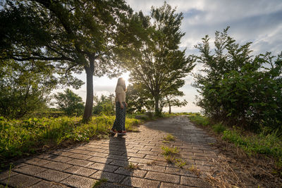 Woman standing on footpath against trees