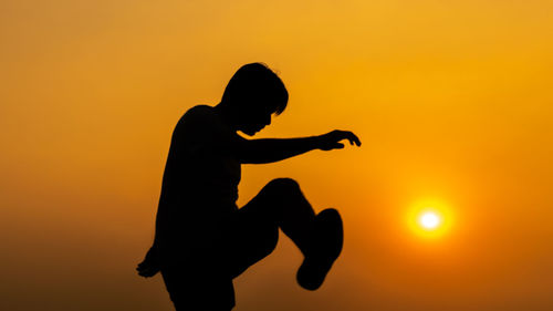 Silhouette man against orange sunset sky