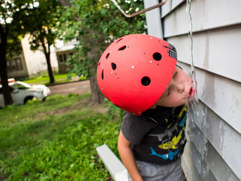 Boy drinking water falling against wall in yard