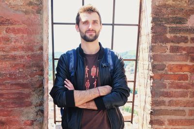 Portrait of young man standing against brick wall