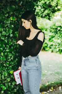 Side view of young woman standing against plants