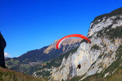 Low angle view of person paragliding by mountains against clear blue sky