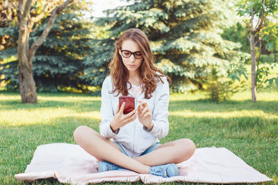 Young woman sitting on field against trees