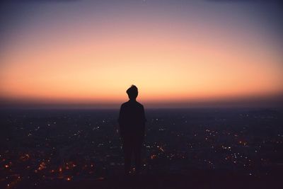 Silhouette of person looking at city view from observation point at sunrise