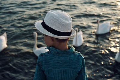 Rear view of boy looking at swan swimming on lake