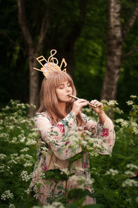Young woman with eyes closed playing flute while standing in forest