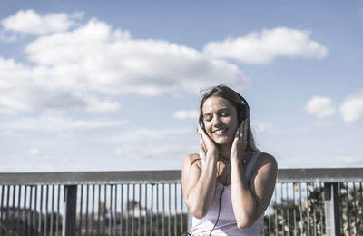 Young woman listening to music against sky