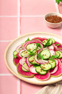 Healthy vegan salad with watermelon radish, cucumber and red onion on pink tile background.