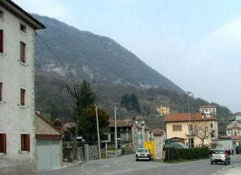 Cars on road by buildings and mountains against sky