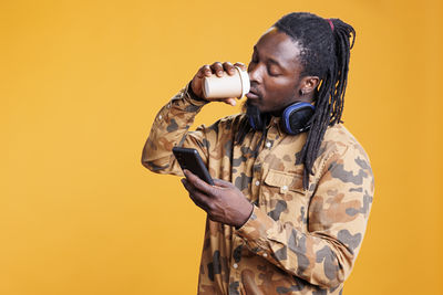 Side view of senior man drinking water against yellow background