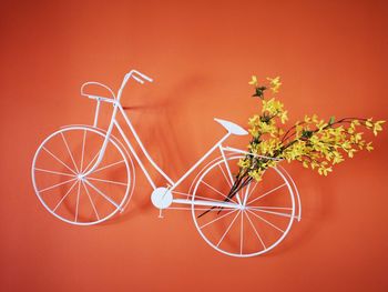 Close-up of flowers i toy bicycle against orange wall