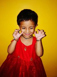 Smiling girl gesturing while standing against yellow background