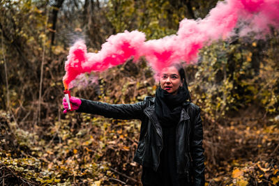 Young woman holding distress flare while standing in forest during autumn