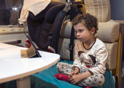 boy inside motorhome entertaining himself by looking at tablet while sitting in pajamas