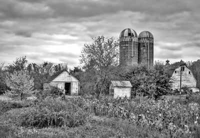 Barn and silos on field against cloudy sky