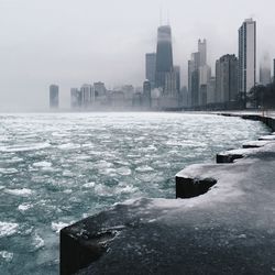 Scenic view of frozen river in city against sky during winter