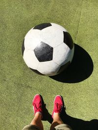 Low section of man standing by large soccer ball on field