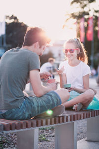 Brother and sister having ice cream while sitting in city