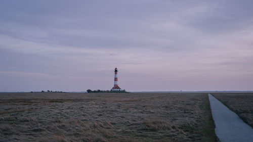 Lighthouse on field by building against sky