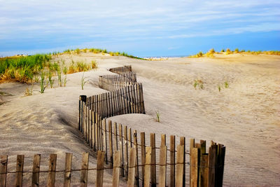 Wooden fence on sandy beach against sky