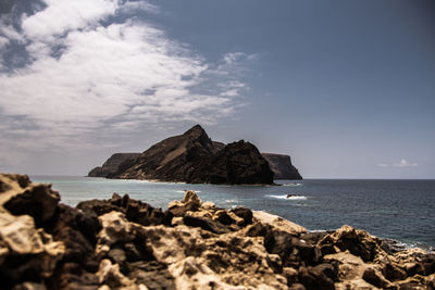 Rocks on shore by sea against sky