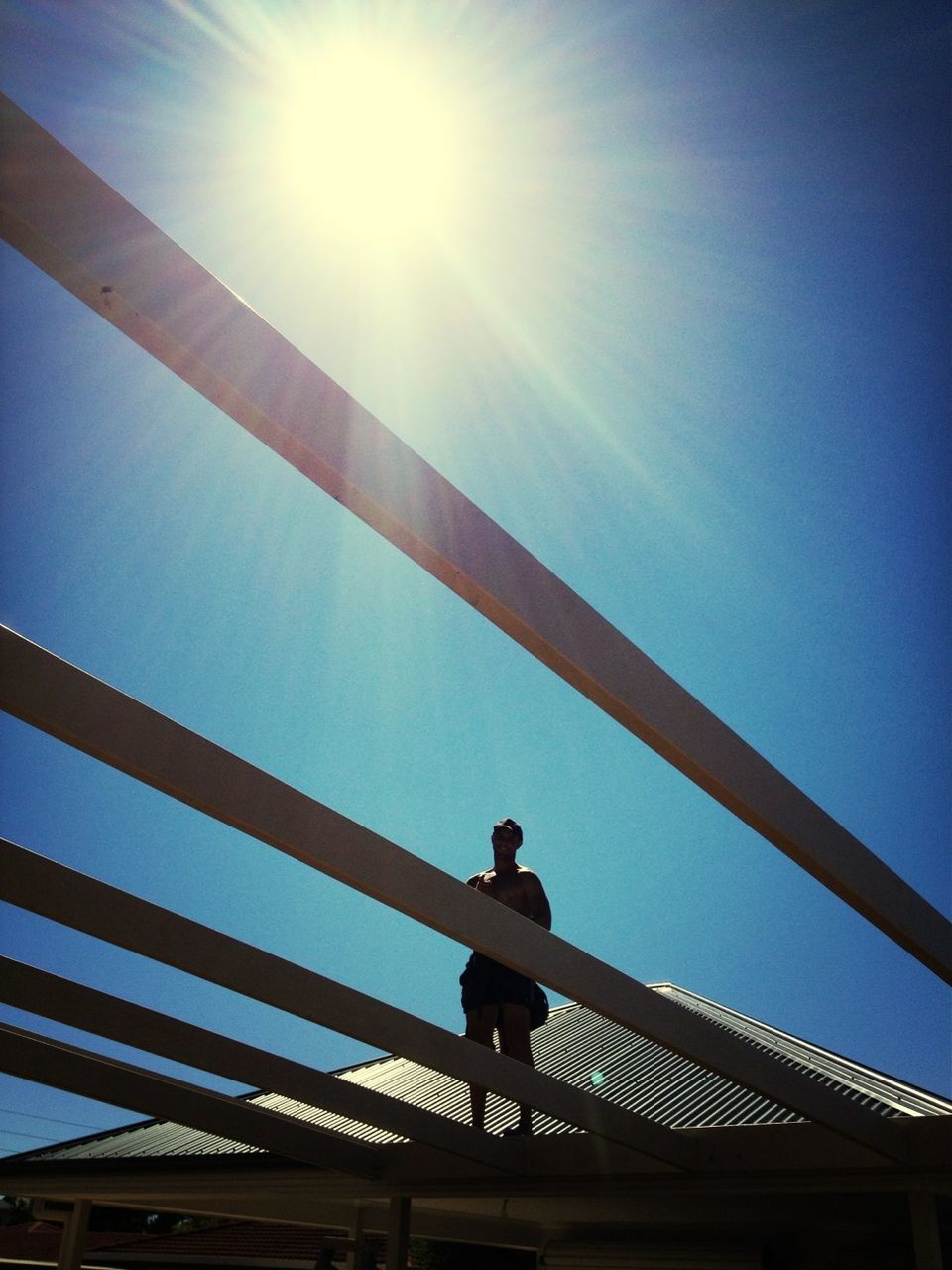 low angle view, built structure, architecture, bridge - man made structure, sun, railing, sunlight, connection, clear sky, sunbeam, silhouette, engineering, blue, lens flare, sky, bridge, lifestyles, standing