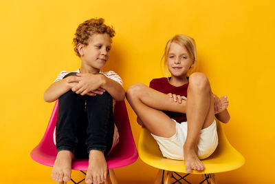 Portrait of smiling young woman sitting against yellow background