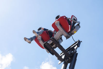 Low angle view of man sitting on amusement park ride against sky
