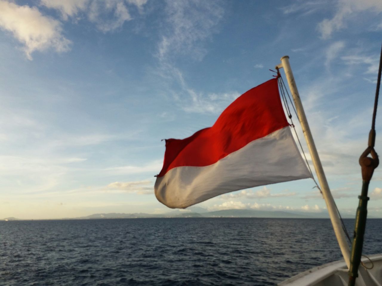 flag, red, patriotism, sea, sky, identity, national flag, water, tranquility, nautical vessel, cloud, horizon over water, cloud - sky, wind, nature, american flag, beauty in nature, tranquil scene, boat, scenics