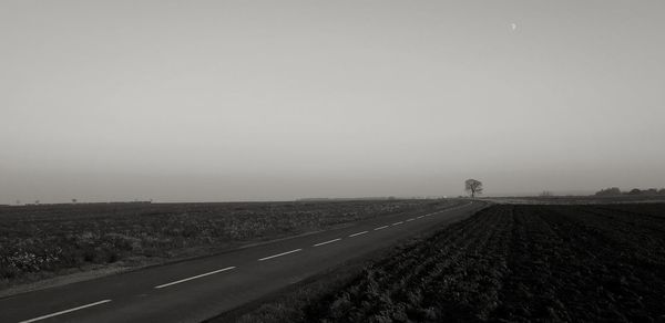 Road amidst field against sky during foggy weather